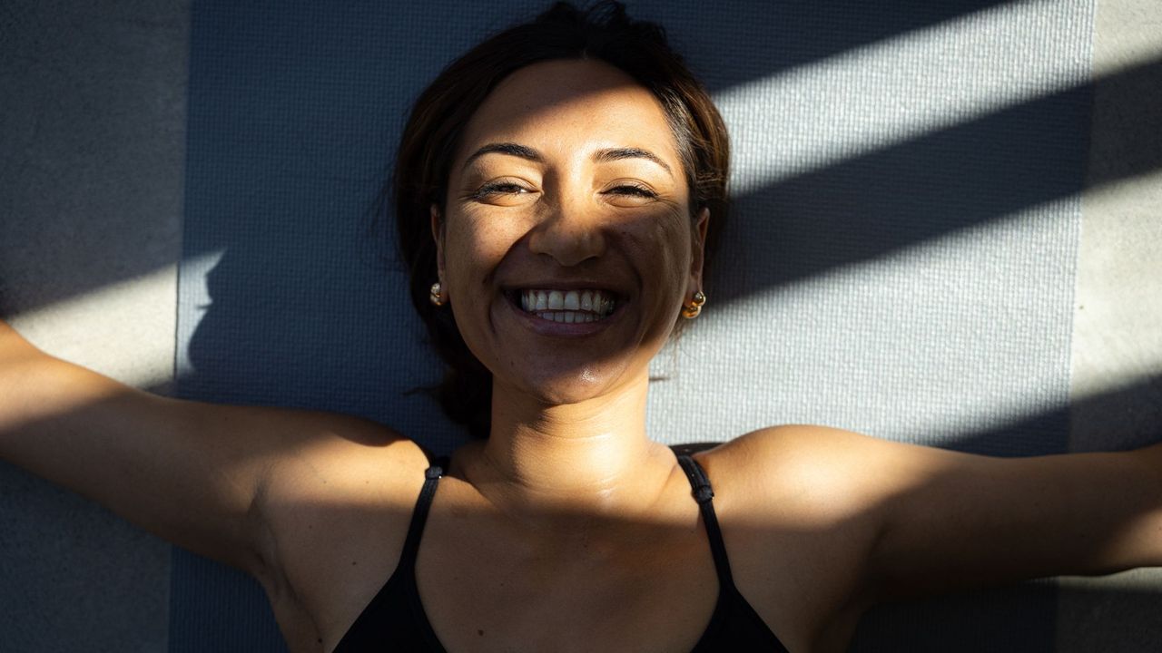 Let Them theory: A woman smiling in the sunshine on a yoga mat