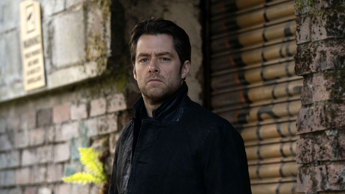 Richard Rankin in a dark jacket as Rebus stands in an alleyway in Rebus.