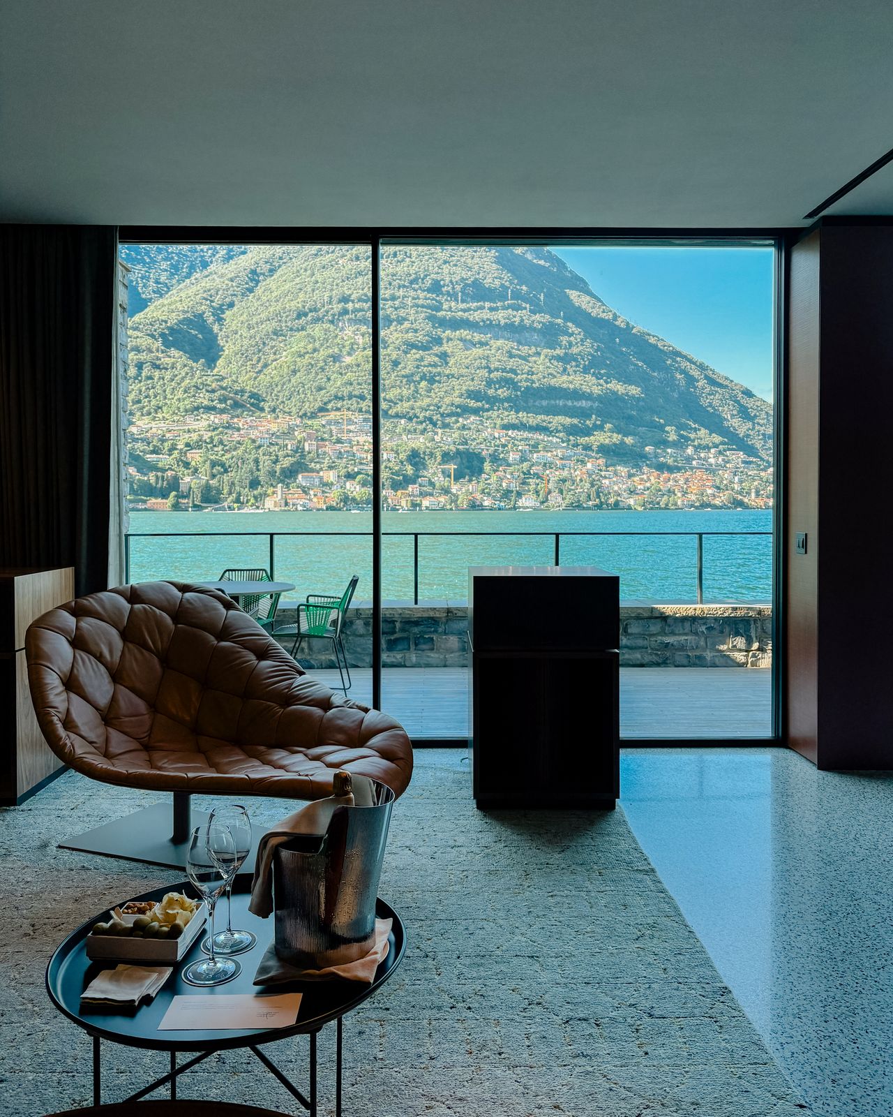 A high-fidelity listening suite fitted with retro-inspired music gear features floor-to-wall windows capturing the natural beauty of a lake and mid-century furniture with natural hues and textural furnishings.