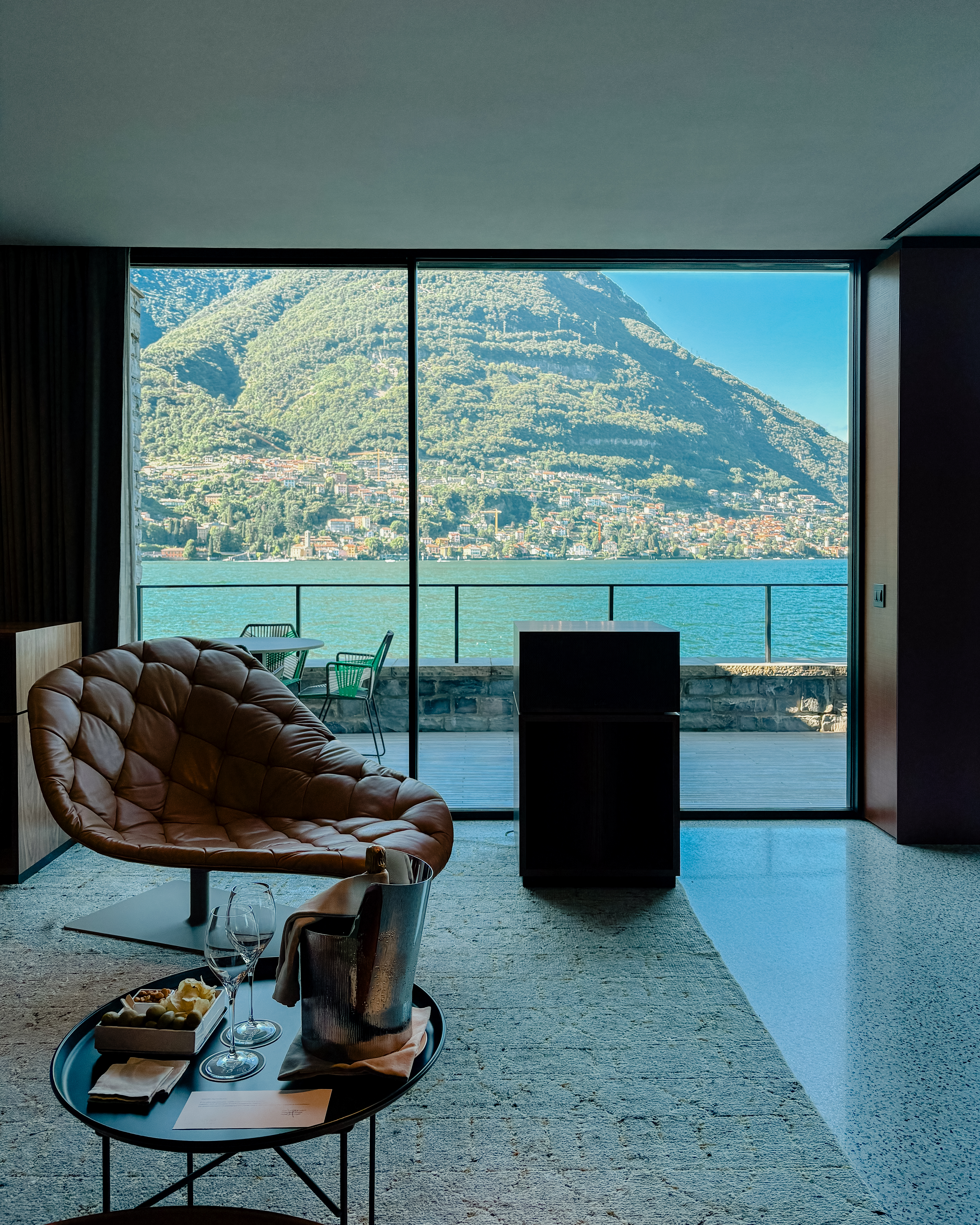 A high-fidelity listening suite fitted with retro-inspired music gear features floor-to-wall windows capturing the natural beauty of a lake and mid-century furniture with natural hues and textural furnishings.
