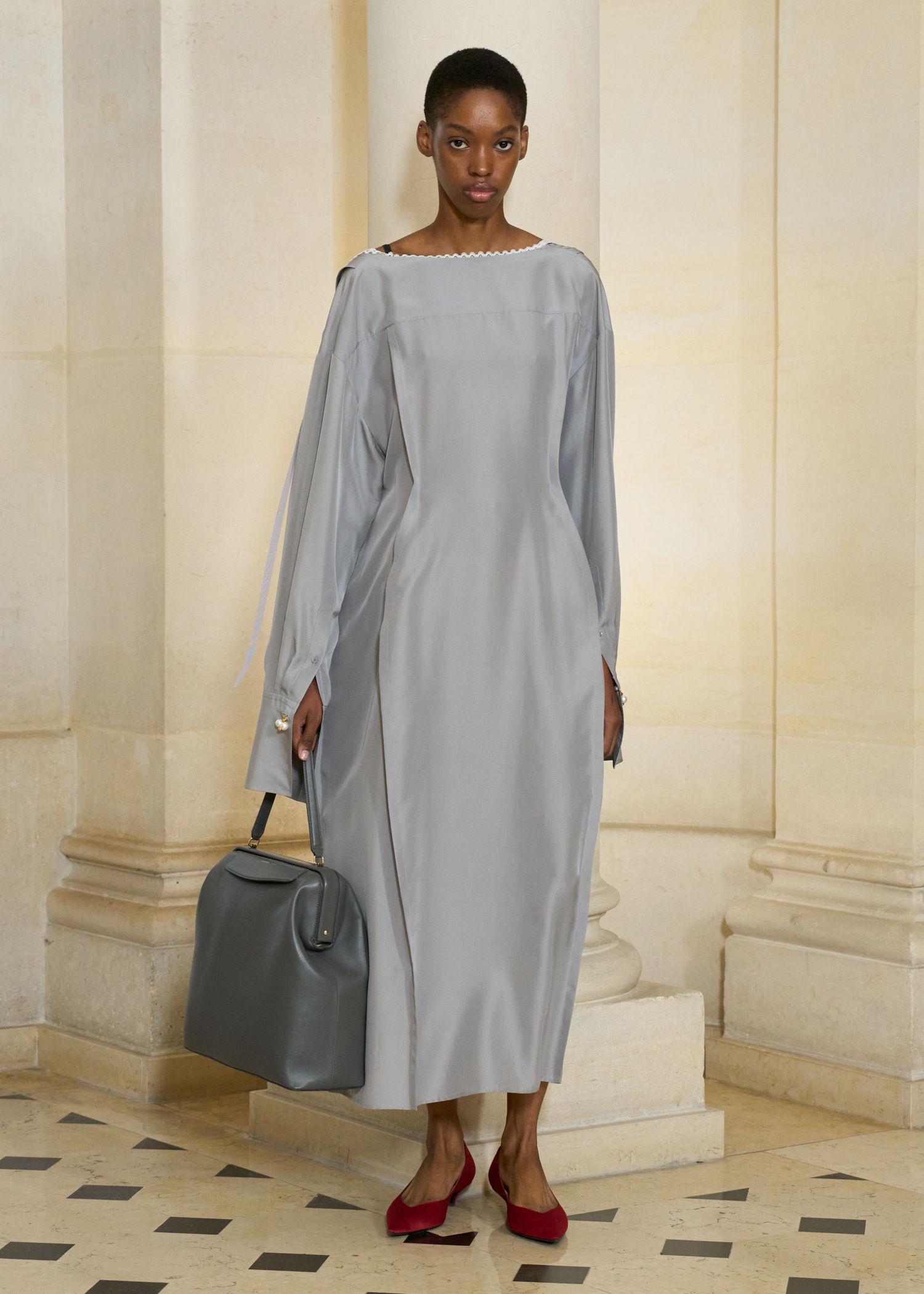 A model in the Carven S/S 26 show wearing a gray dress with a dark gray kiss-lock bag.