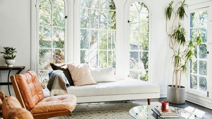 A living room with a large window, a white sofa, and two leather chairs
