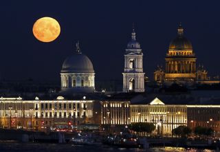 Полная луна светит над церковью Святой Екатерины (слева) и Исаакиевским собором в Санкт-Петербурге, Россия, 21 августа 2021 года.