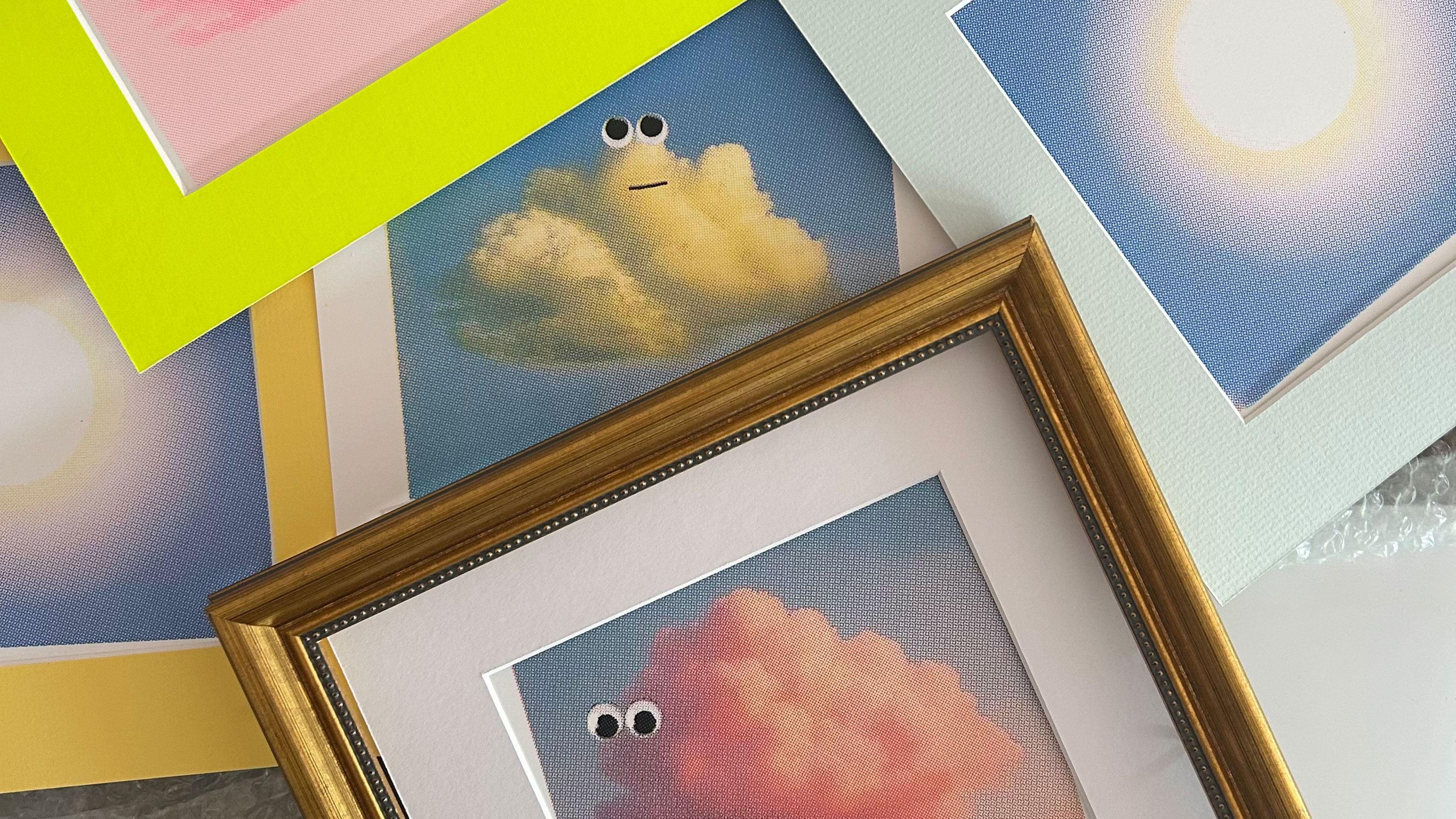 Collection of mounted and framed screen prints of clouds with googly eyes