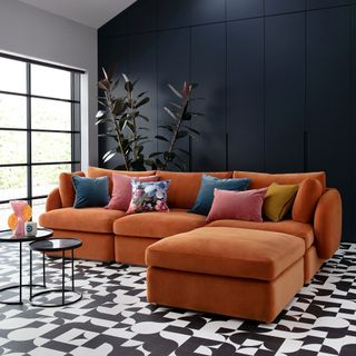 Orange L-shaped sofa in front of a dark blue painted panelled wall in a room with monochrome geo tiled floor