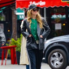Jennifer Lawrence walking in the street wearing track pants, a green cardigan, and leather blazer.