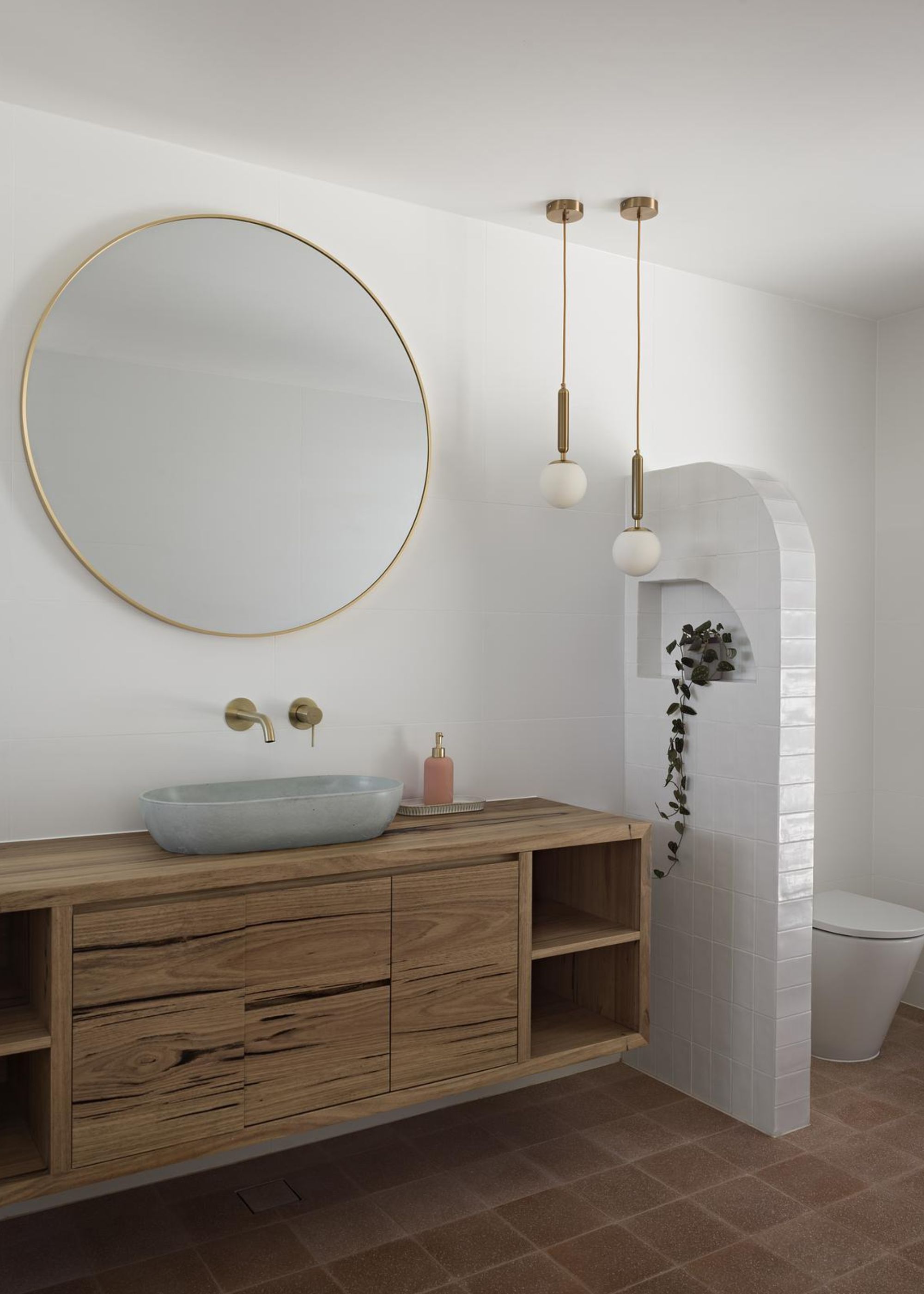 A bathroom that has been zoned up into two. On one side is the basin and bathroom, vanity with a mirror above it and on the other side behind a small curved wall is a toilet.
