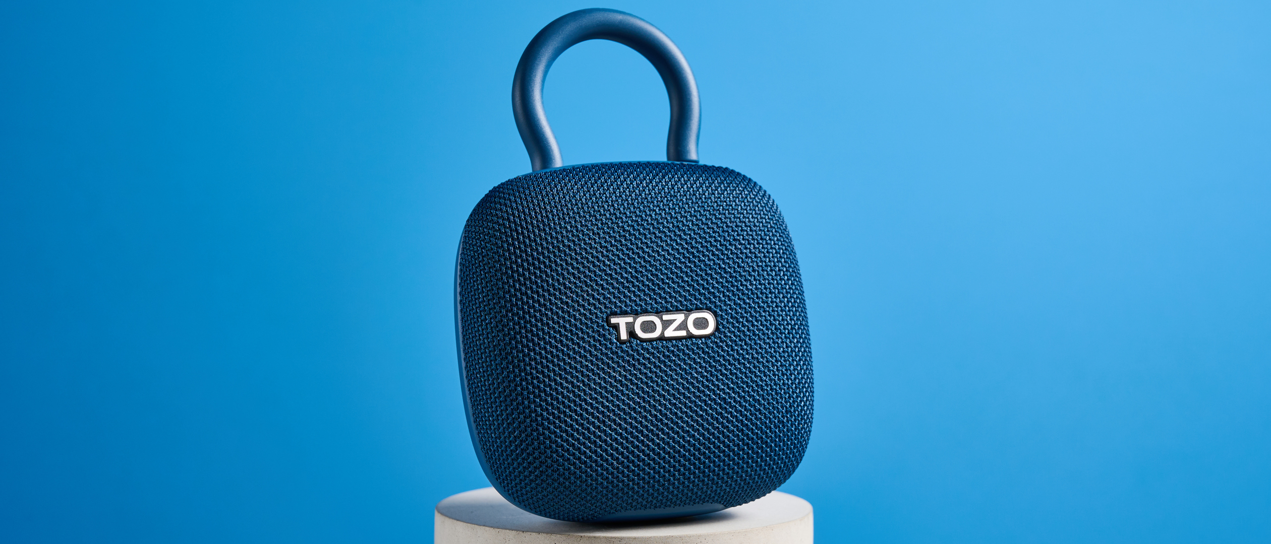 Tozo PE1 speaker in blue with built-in clip photographed on a blue background.