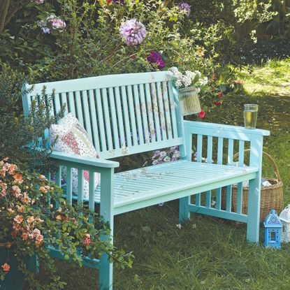 A turquoise-painted garden bench surrounded by flowering plants