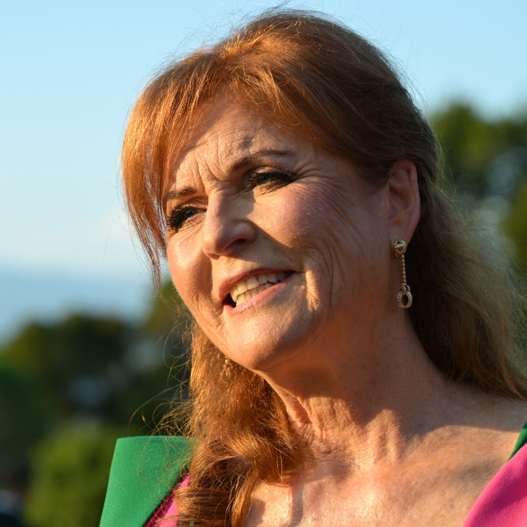 Sarah Ferguson smiling outside in a green and pink dress