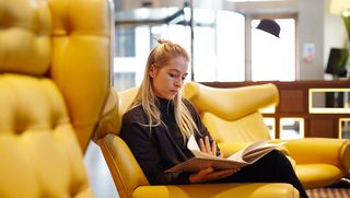 Artist reading a book in lobby on yellow chair