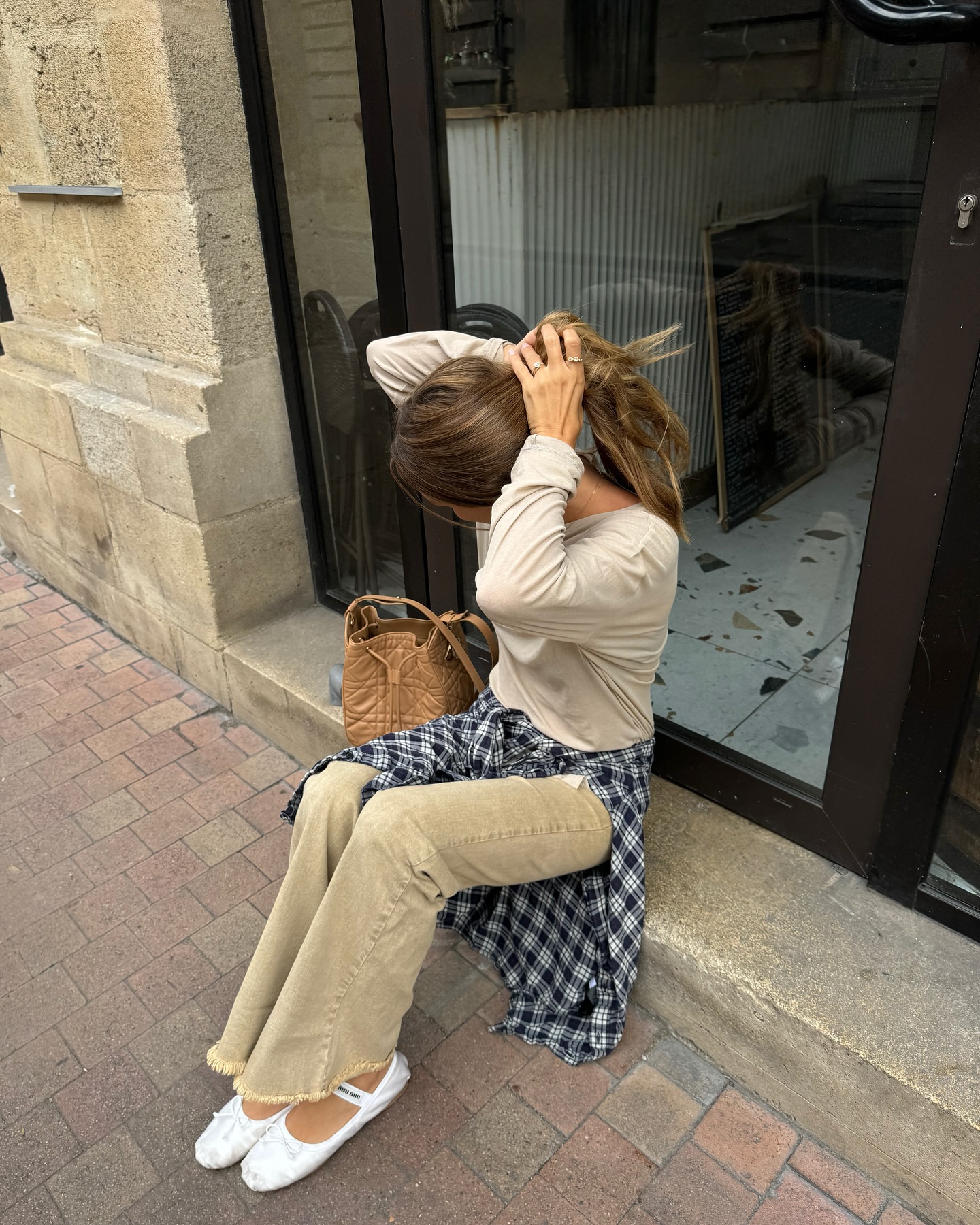 @annelauremais wears a ballet flat outfit consisting of white satin ballet flats from Miu Miu, beige coloured jeans, a checked shirt and a crew neck shirt.