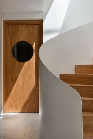 White hallway with oak wood stairs and door with porthole window