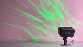 The Govee Outdoor Projector Light is projecting a green aurora image onto a pink wall.