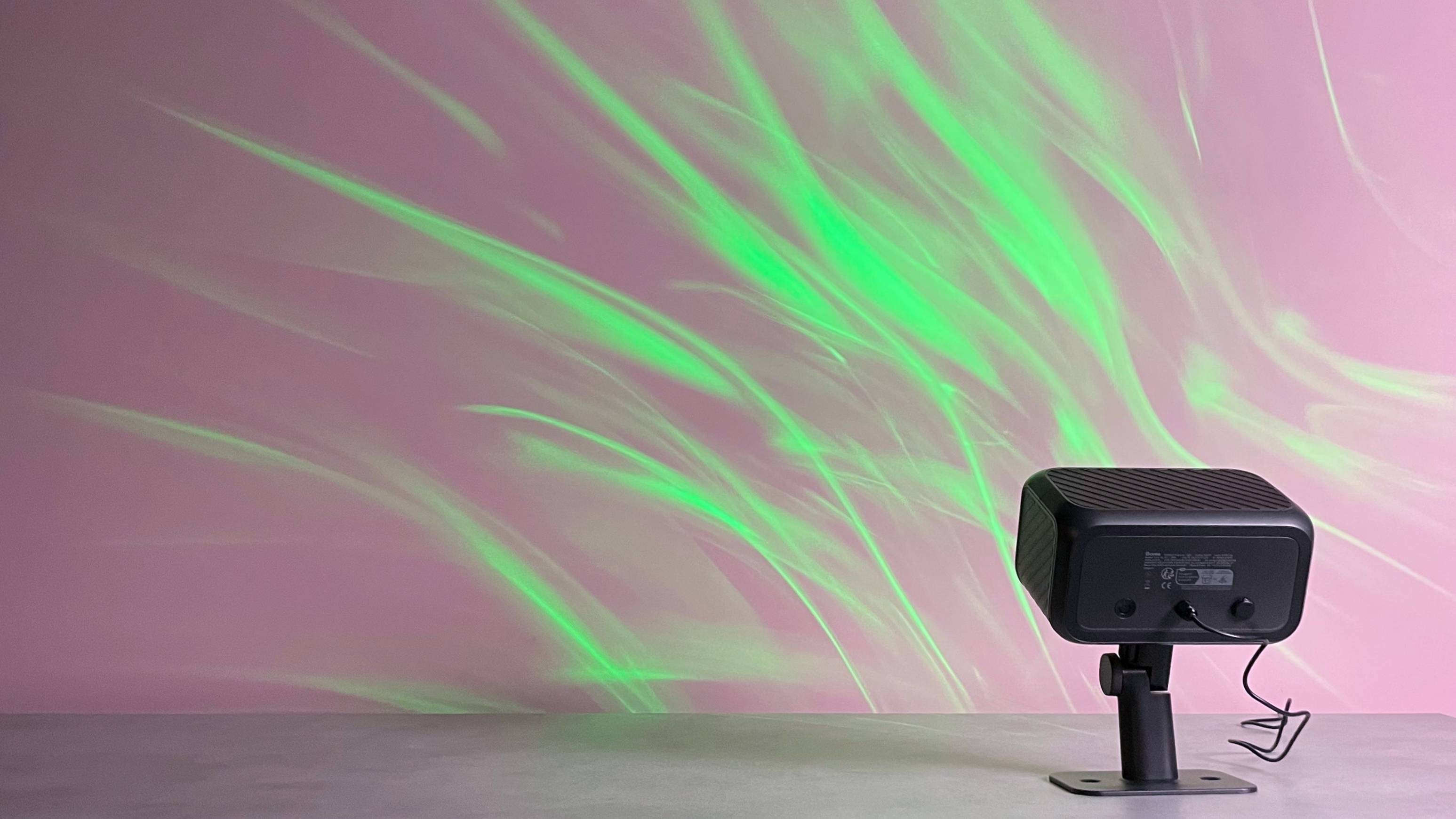 The Govee Outdoor Projector Light is projecting a green aurora image onto a pink wall.