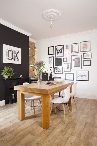 dining room with a black feature wall and a gallery wall wiith a wooden table and wooden flooring