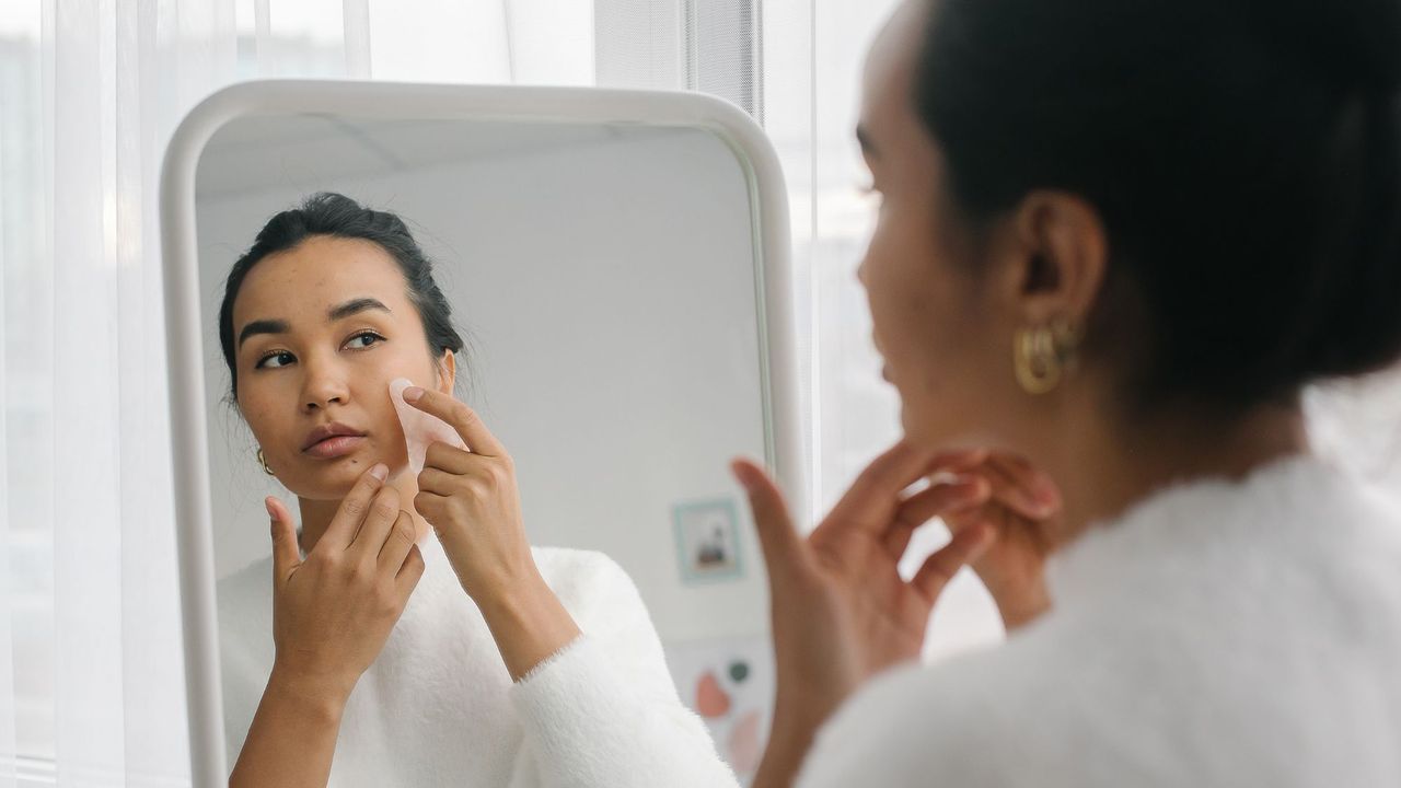 Gua sha routine - woman doing gua sha in the mirror