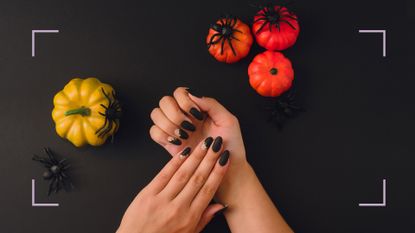 a woman&#039;s hands wearing halloween nail designs on black background with pumpkins