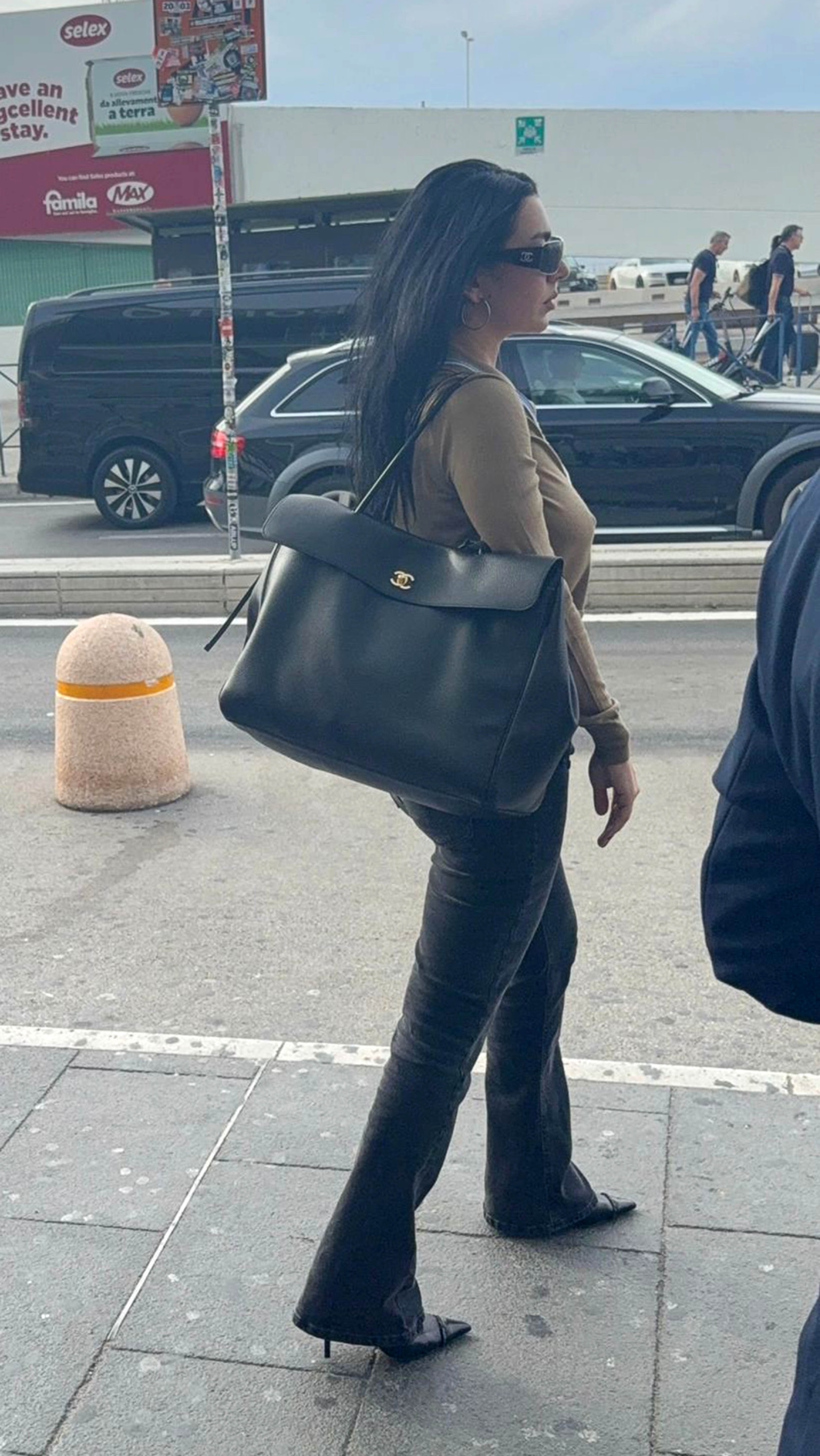 Charli XCX gets of an airplane wearing black flared jeans with heels pointed-toe boots and a large Chanel bag.