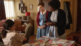 Shelagh (Laura Main) and Joyce (Renee Bailey) in uniform speak to a mum holding her baby in Call the Midwife.