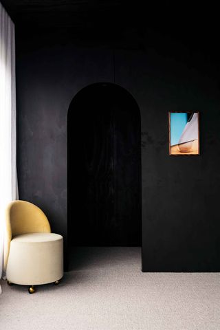 Black-stained walls and a cream two-tone chair next to an archway
