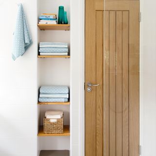 bathroom with shelves next to a door with towels and storage baskets