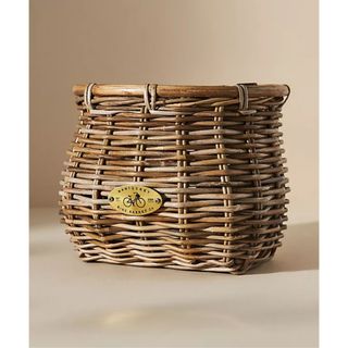 A woven bike basket with a small metal plaque engraved with a bike on the front. 