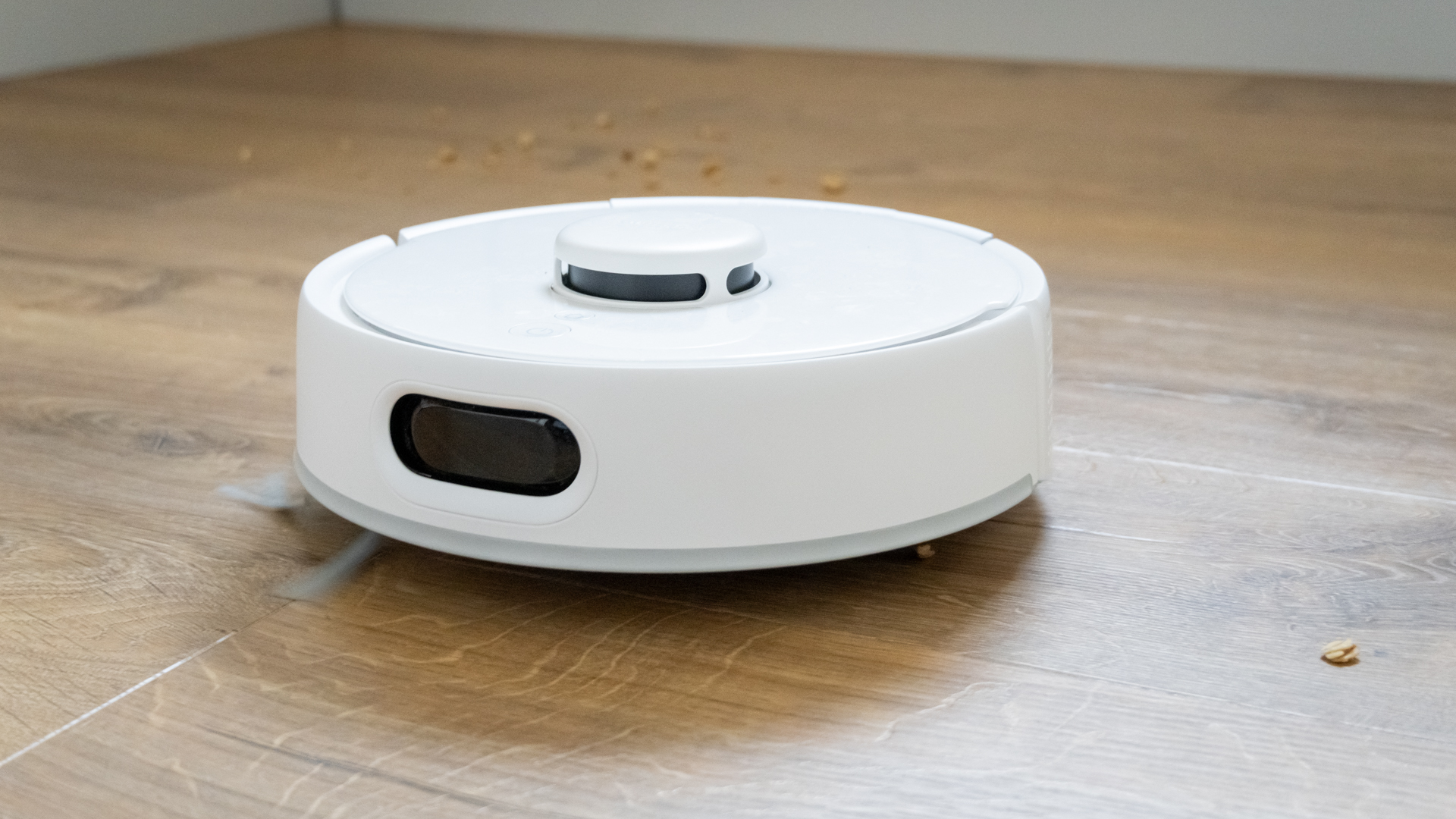 SwitchBot K10+ Pro mini robot vacuum on hard floor, with crumbs from pickup tests alongside