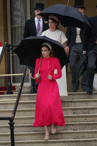 Princess Beatrice exits a building wearing a hot pink dress under an umbrella