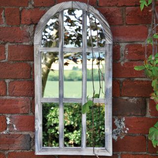garden mirror with distressed wooden frame on old brick garden wall