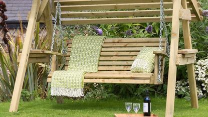 a garden swing set in the garden with glasses and bottle of wine on the grass