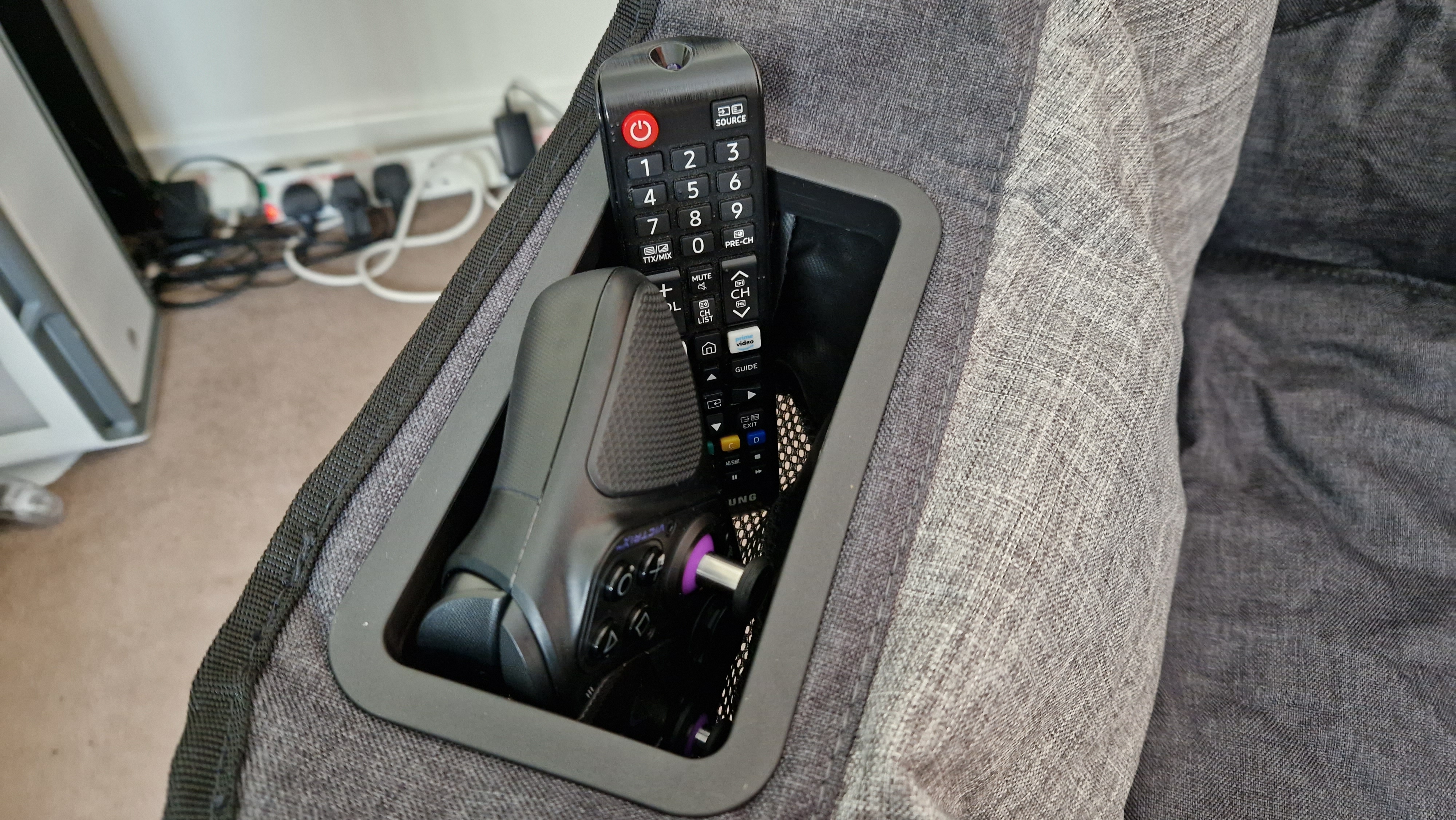The Foldable Gaming Chair's pouch pocket carrying a Victrix Pro BFG PS5 controller, and a Samsung TV remote