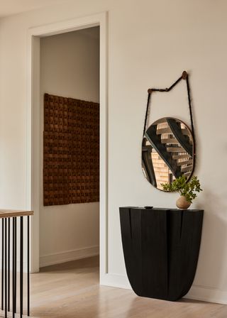 A stair-side home nook with a dark side table and a hanging mirror