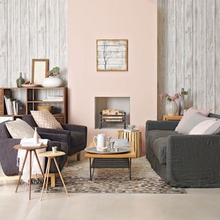 A living room with pale pink chimney breast wall with faux wood wallpaper in alcoves either side with dark grey sofas