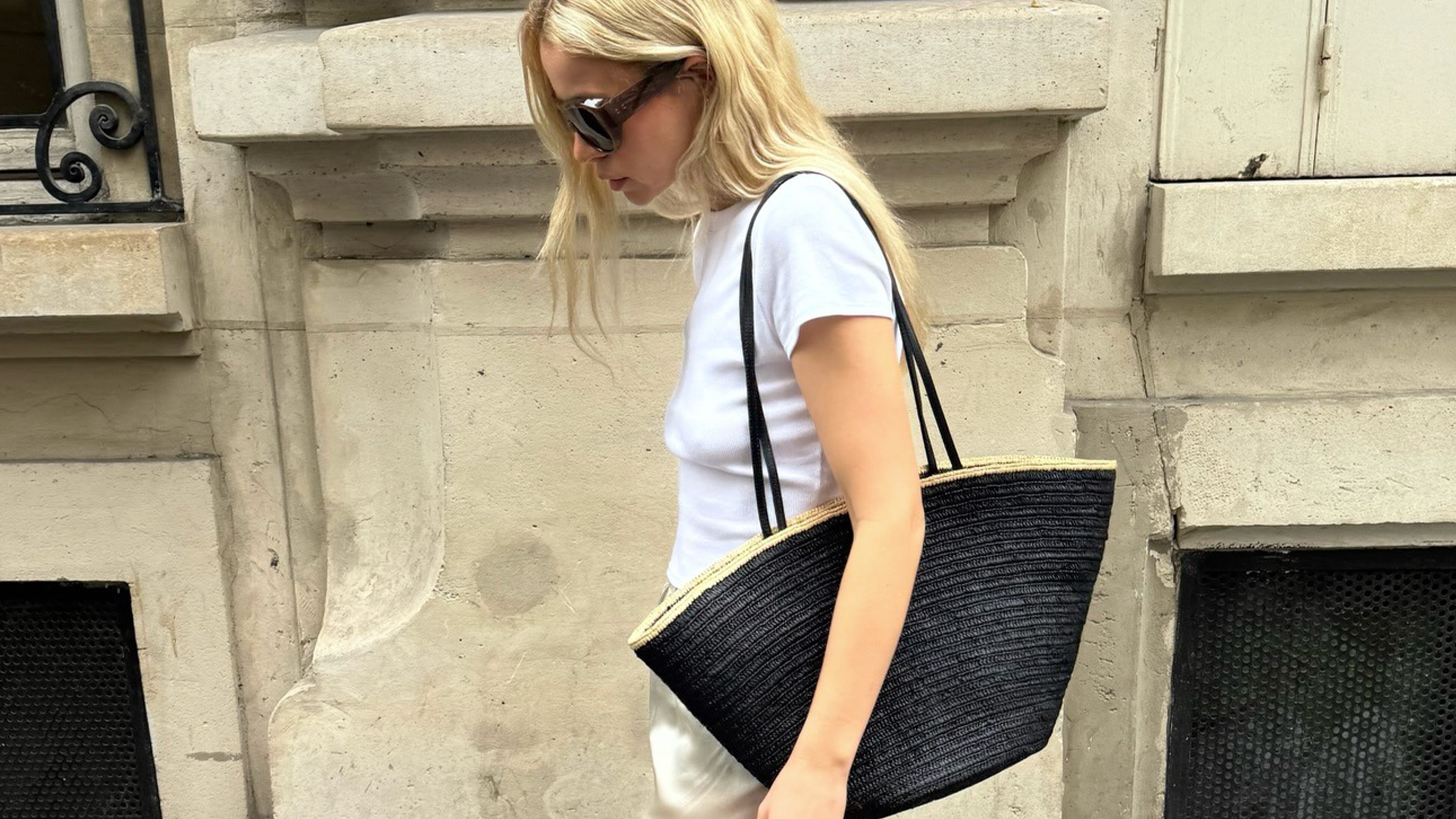 Photo of influencer wearing a spring 2026 outfit with satin pants, featuring white t-shirt, black raffia tote bag, and ivory satin pants.