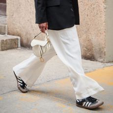Woman wearing white trousers, Adidas sneakers, and a Dior saddle bag