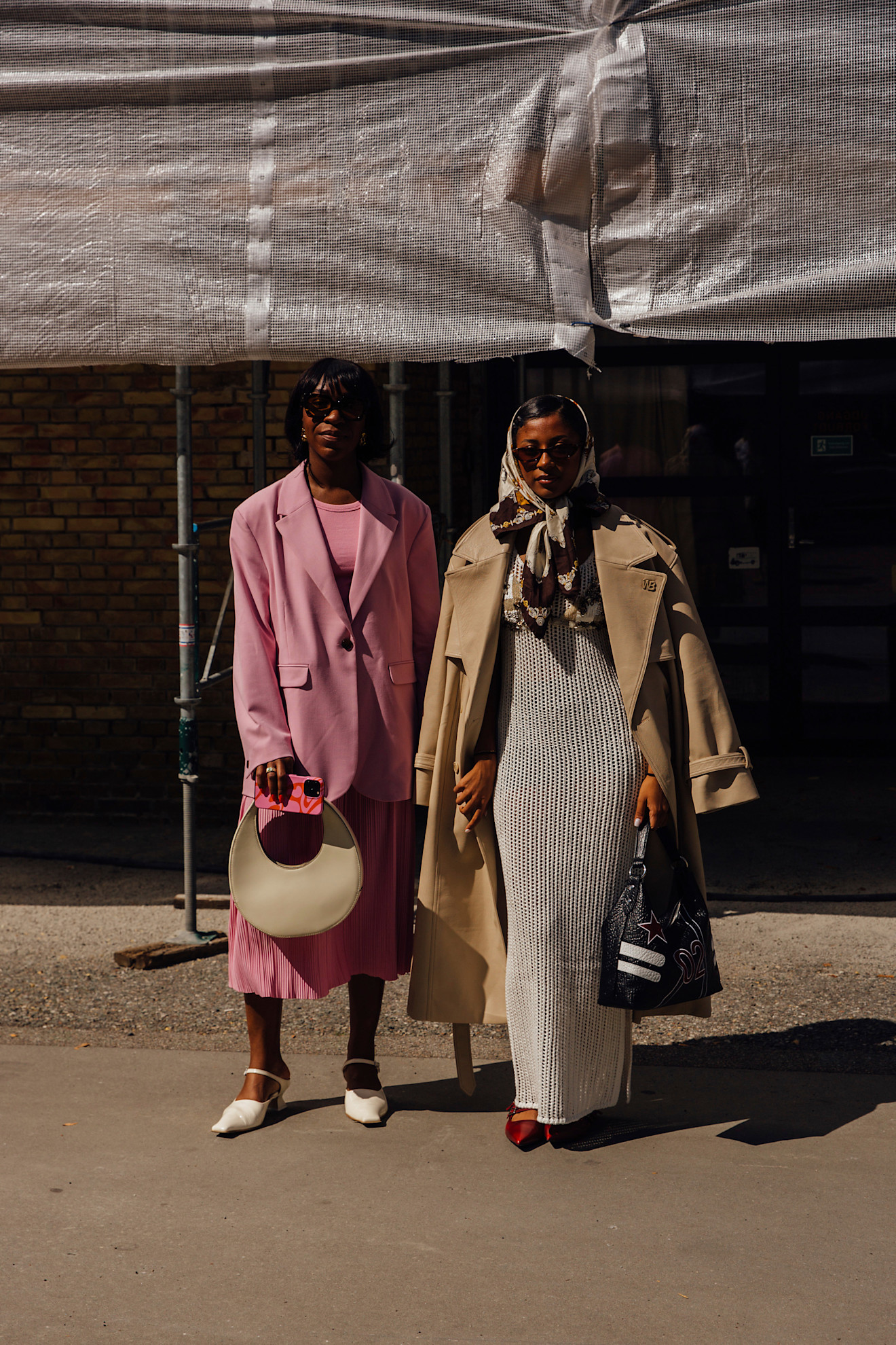 woman wearing pink blazer, pink dress, beige bag, and white heels; woman wearing beige jacket, gray dress