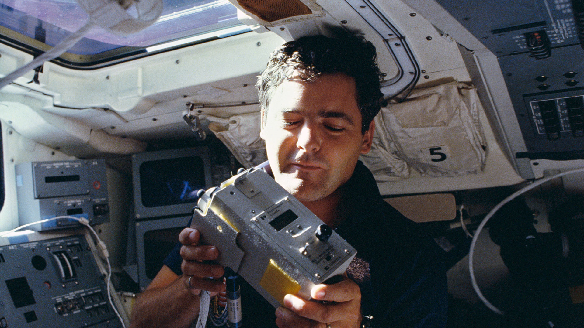 A man works with a scientific instrument aboard a spacecraft