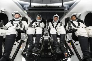 four astronauts in spacesuits sitting in a spacecraft