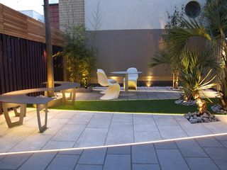 a modern paved, zoned garden with a white dining set and palm tree-esque trees on the borders