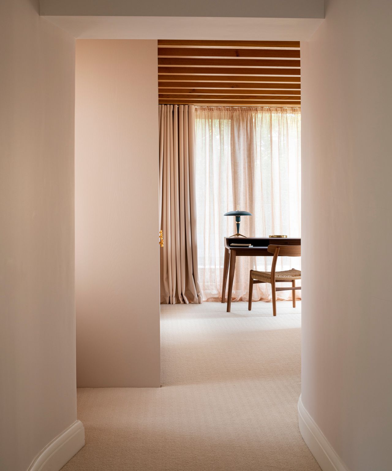 neutral hall looking through to beamed room with wooden desk and wooden chair