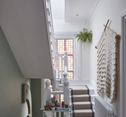White painted staircase with neutral stair carpet and long red framed stained glass window 
