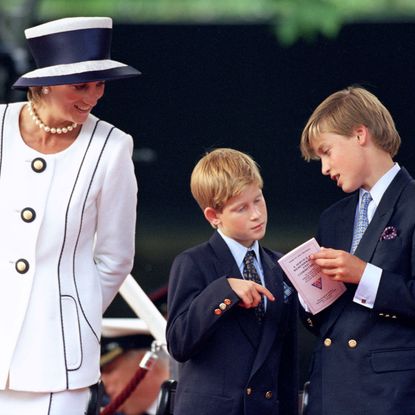 Princess Diana wearing a white suit and hat smiling at Prince Harry and Prince William, who are looking at a program