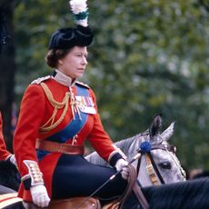 Queen Elizabeth wearing a red uniform riding a horse