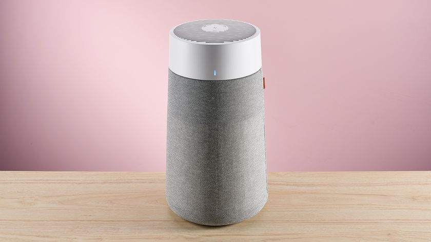 The large Blueair air purifier sits facing forward on a wood surface against a pink background.