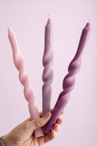 A woman's hand holding three different colored twisted candles in pink and purple colorways