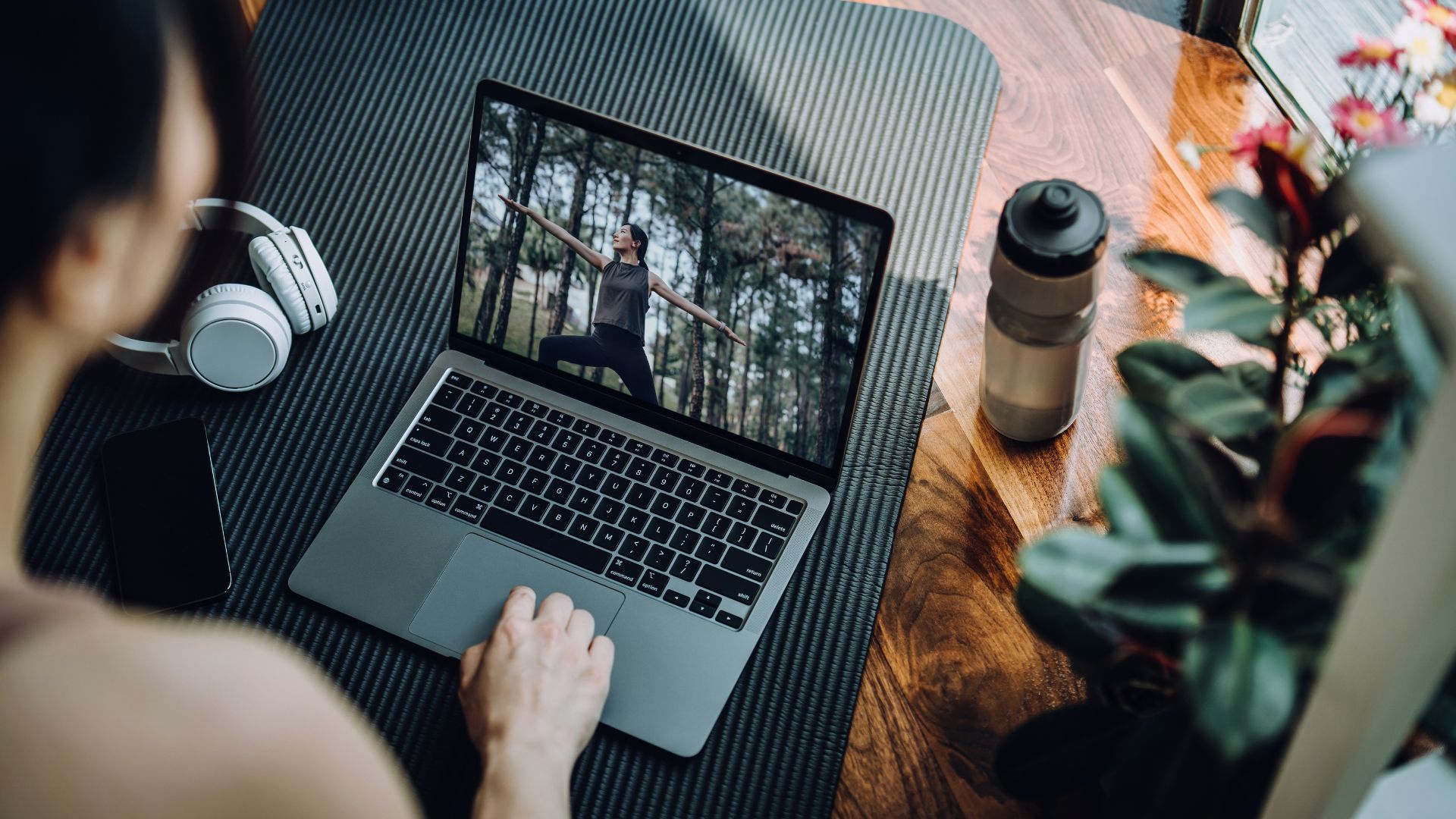 Woman scrolling through the best strength training apps on laptop with water bottle on yoga mat
