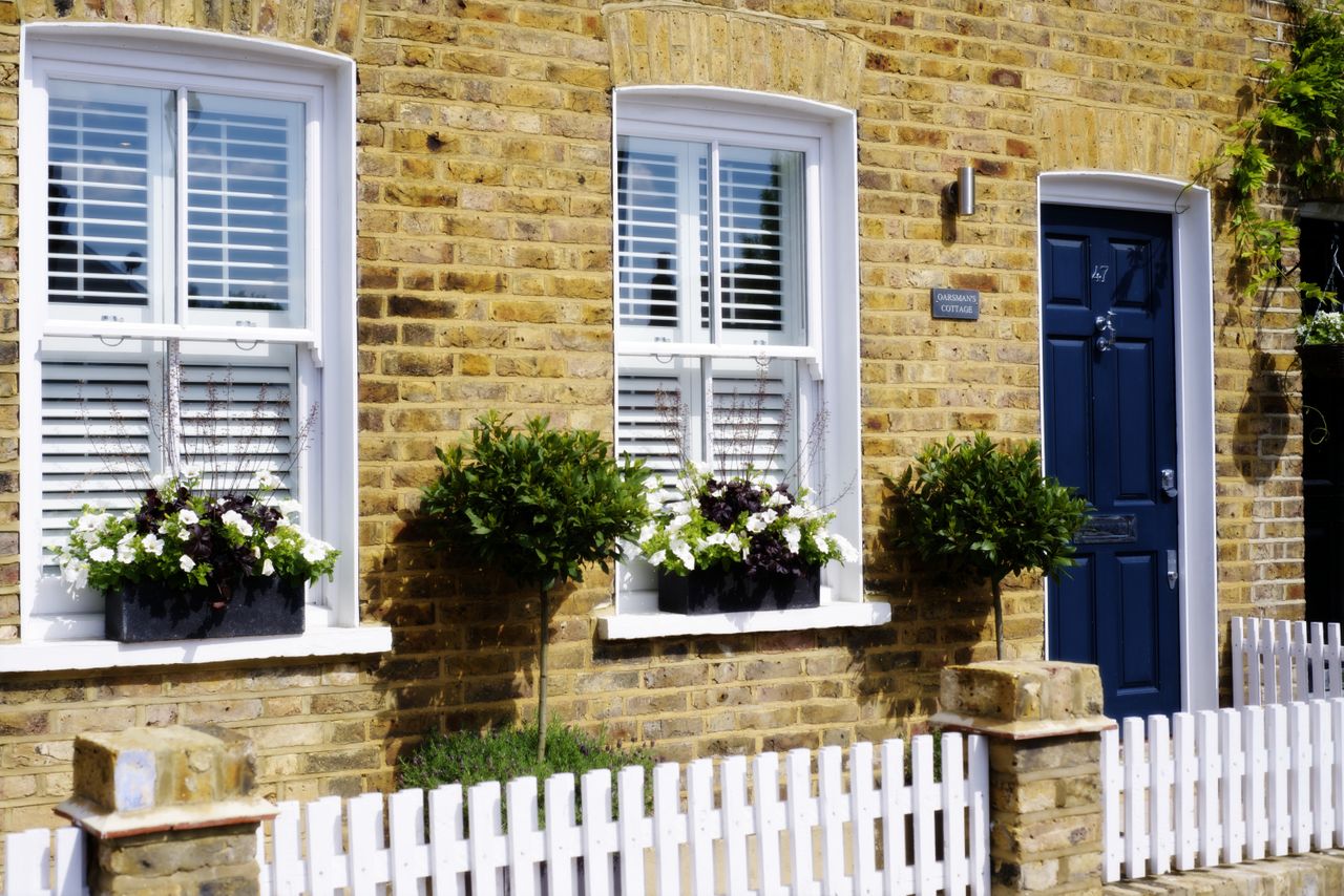 Exterior of brick house with blue front door, white sash window and white picket fence