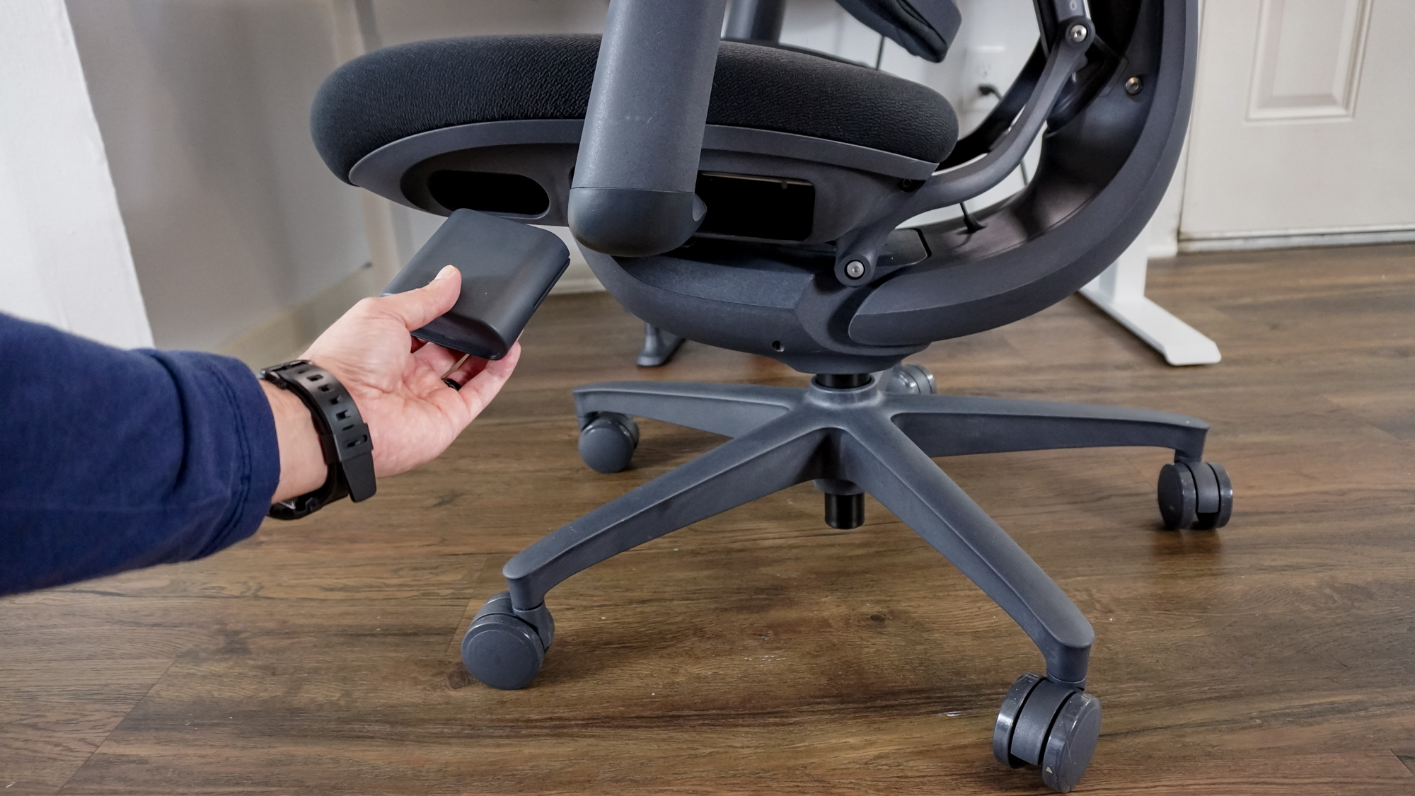 A person installing the battery into the compartment on the underside of the LiberNovo Omni office chair