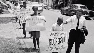 A still from the documentary MLK/FBI in which Martin Luther King stands with people holding protest signs.